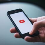 Smartphone in mano con sfondo Youtube