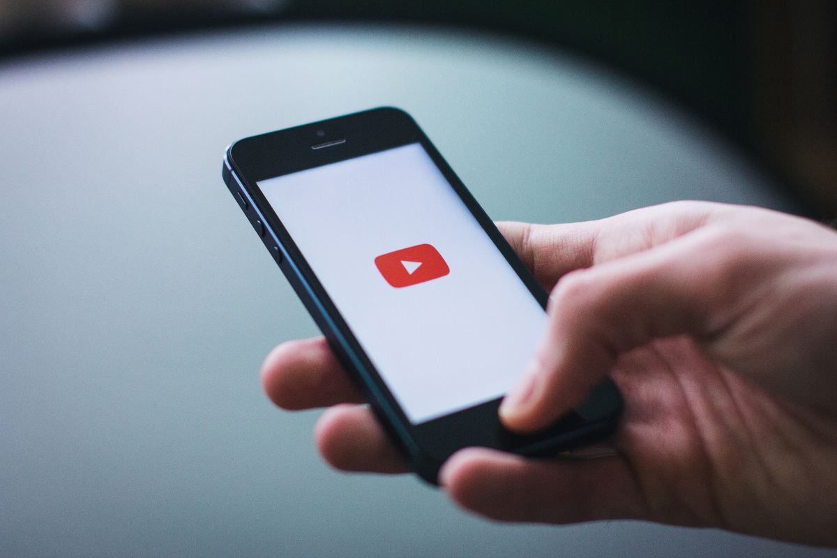 Smartphone in mano con sfondo Youtube