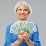 donn anziana sorridente con in mano tante banconote da 100 euro