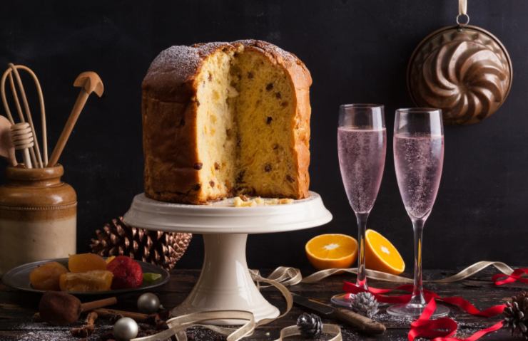 panettone sopra un'alzatina per dolci con accanto due calici di spumante