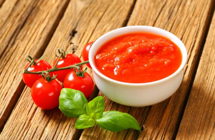 passata di pomodoro dentro ad una ciotola con accanto dei pomodori e del basilico