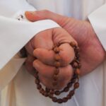 prete con un rosario nelle mani dietro la schiena