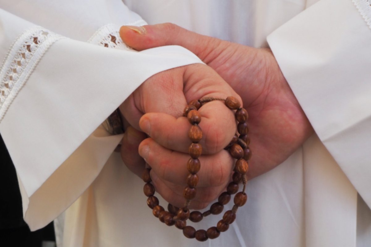 prete con un rosario nelle mani dietro la schiena