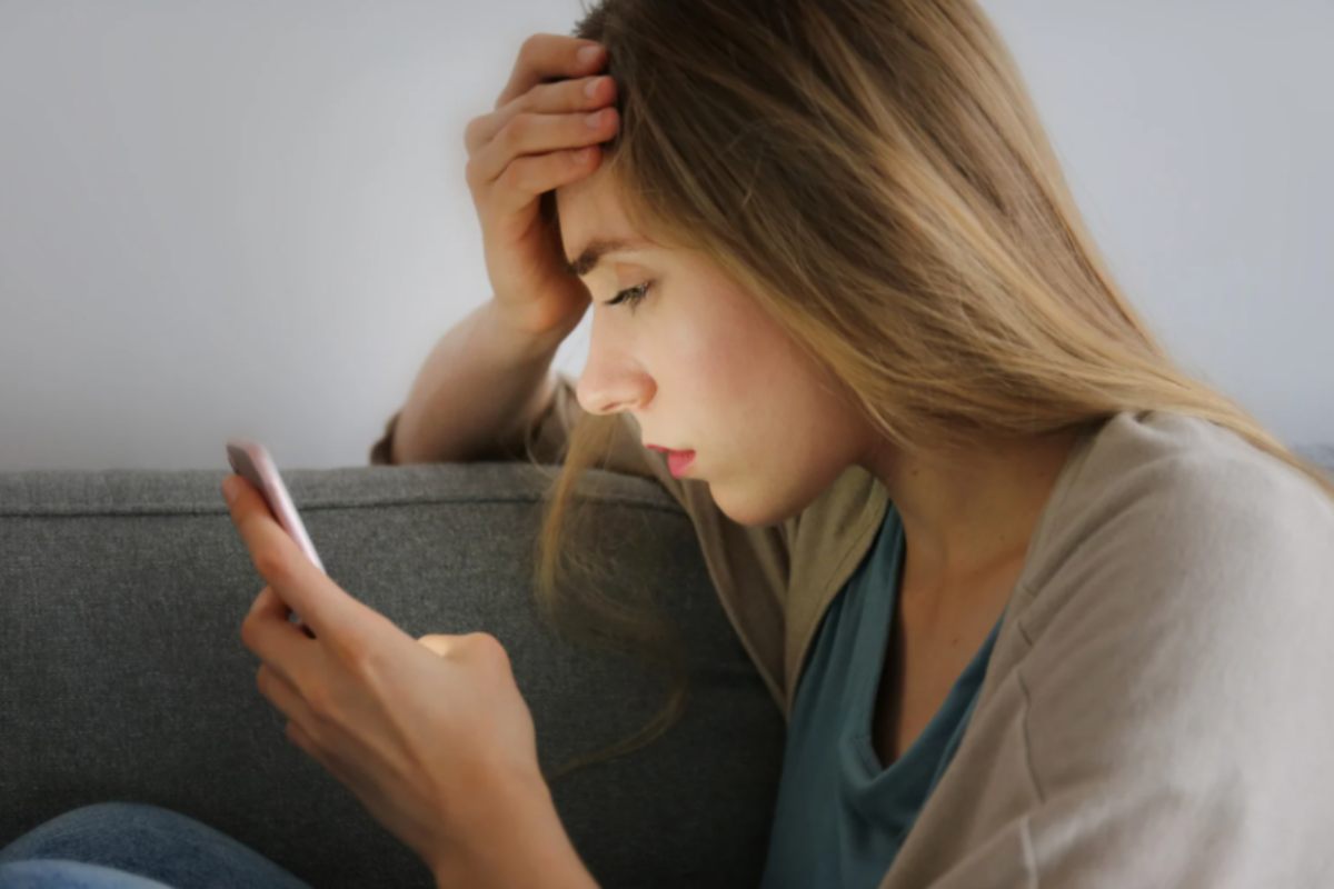 donna preoccupata con una mano sulla fronte e il cellulare nell'altra mano