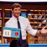 Stefano Der Martino sorridente con un pacco di Affari Tuoi in mano