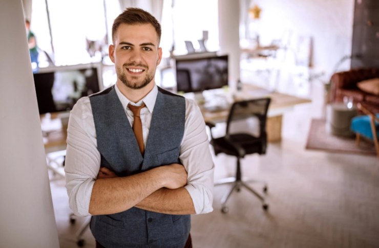 giovane imprenditore che sorride e alle sue spalle dei computer