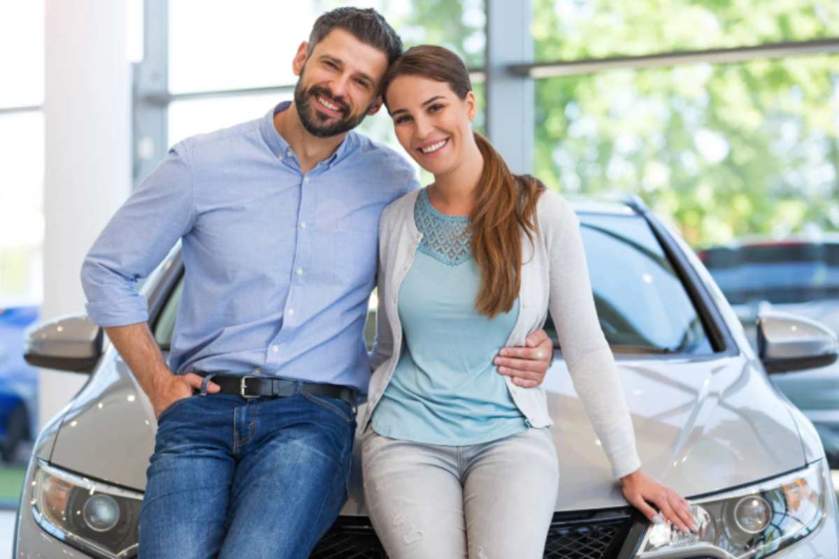 uomo e donna abbracciati e sorridenti appoggiati ad un'auto