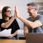 uomo e donna sorridenti davanti al computer che battono il 5 con le mani