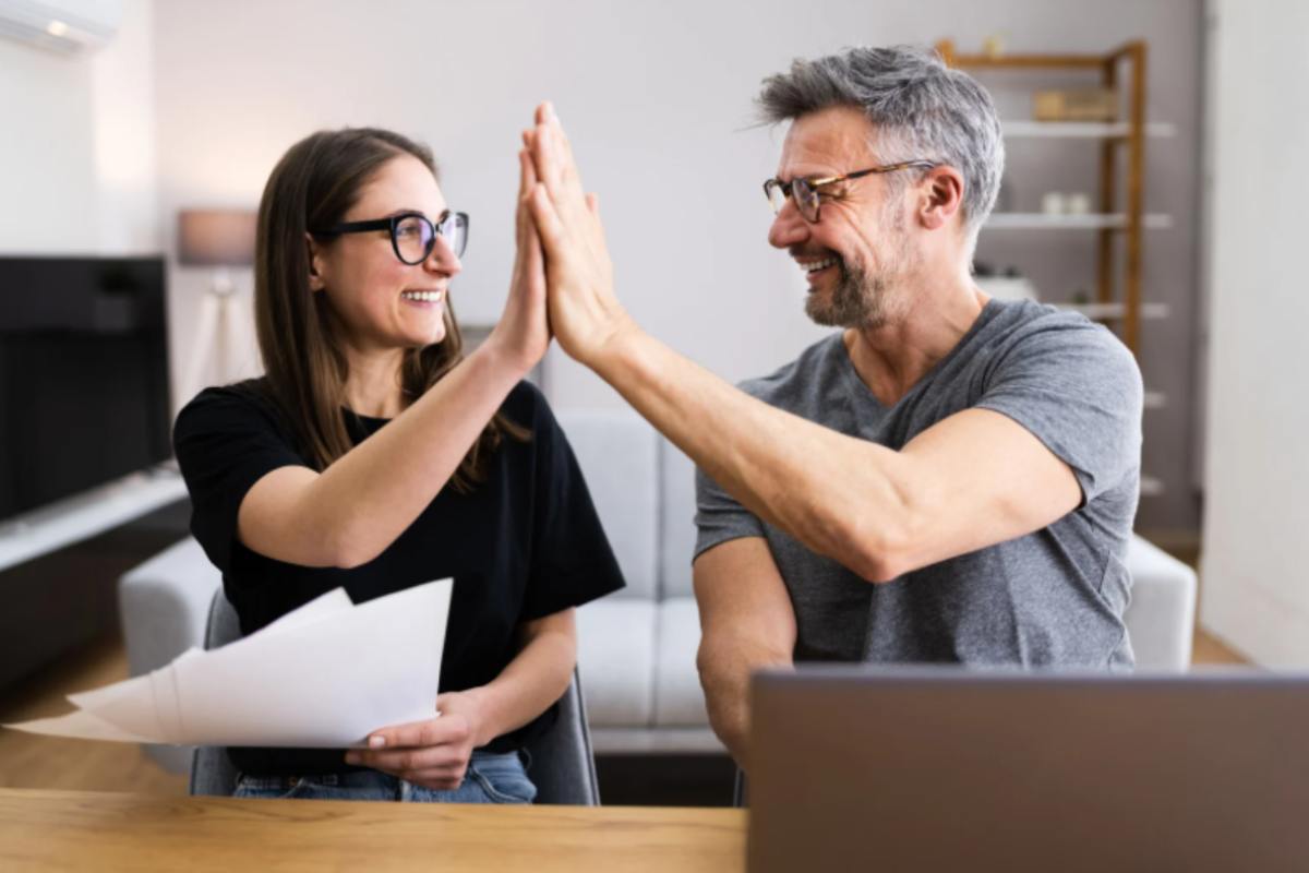 uomo e donna sorridenti davanti al computer che battono il 5 con le mani