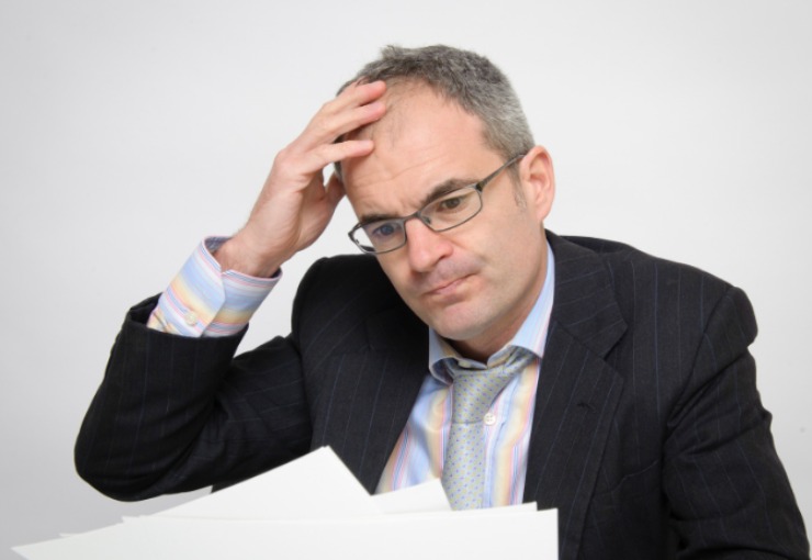 uomo preoccupato che legge dei fogli e si mette una mano sulla testa