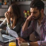 uomo e donna di fronte al computer che leggono dei fogli con espressione preoccupata