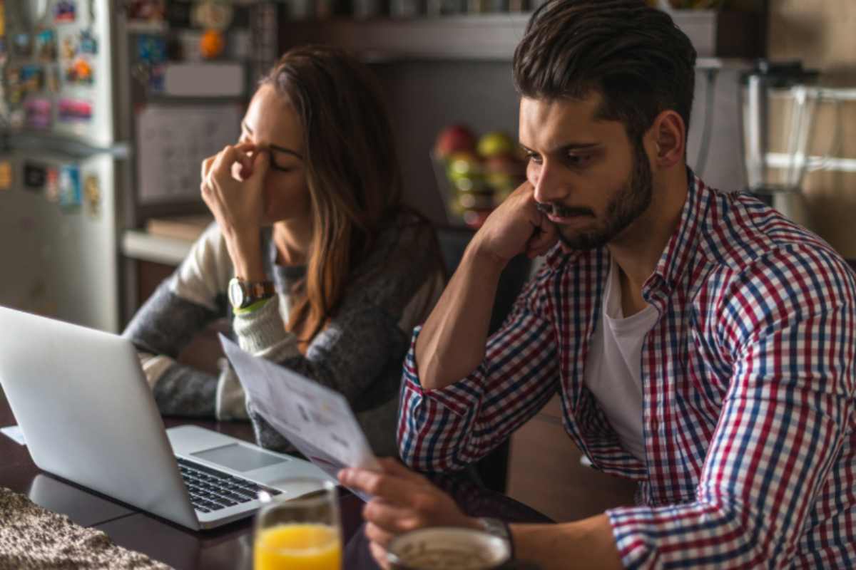 uomo e donna di fronte al computer che leggono dei fogli con espressione preoccupata