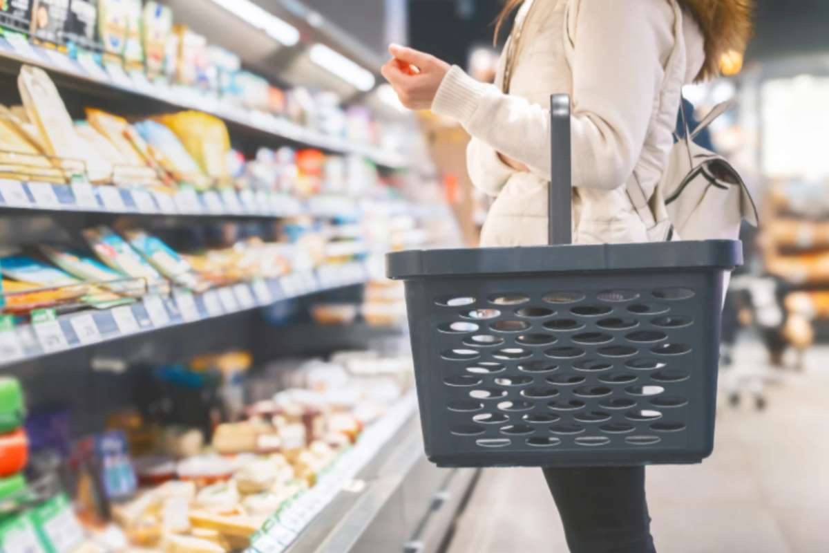 donna al supermercato con il cestino della spesa attaccato al braccio