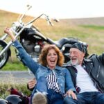 donna e uomo seduti sul ciglio della strada e moto parcheggiata dietro