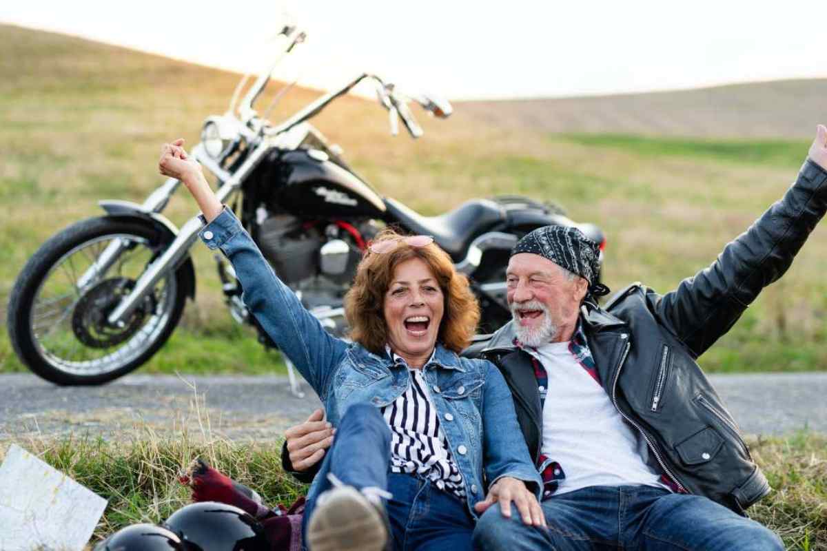 donna e uomo seduti sul ciglio della strada e moto parcheggiata dietro